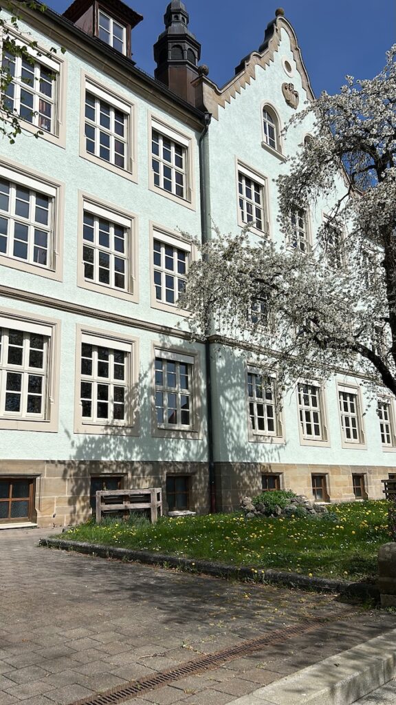 Außenansicht des Schulgebäudes mit einem blühenden Obstbaum im Vordergrund